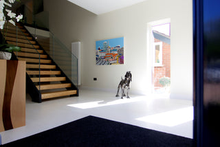 Showcase of painting, metal dog and side table next to stairs inside a modern home